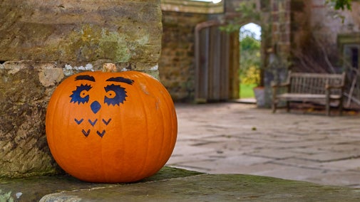 A Pumpkin with a funny face sitting on the ruins wall.